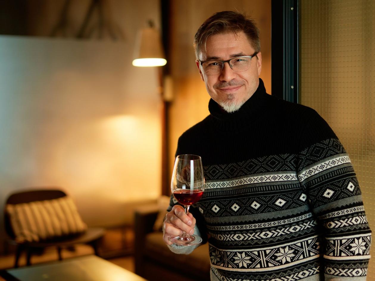 Happy man drinking wine in winter holding wine glass, smiling. Wine tasting at home. Portrait of mat