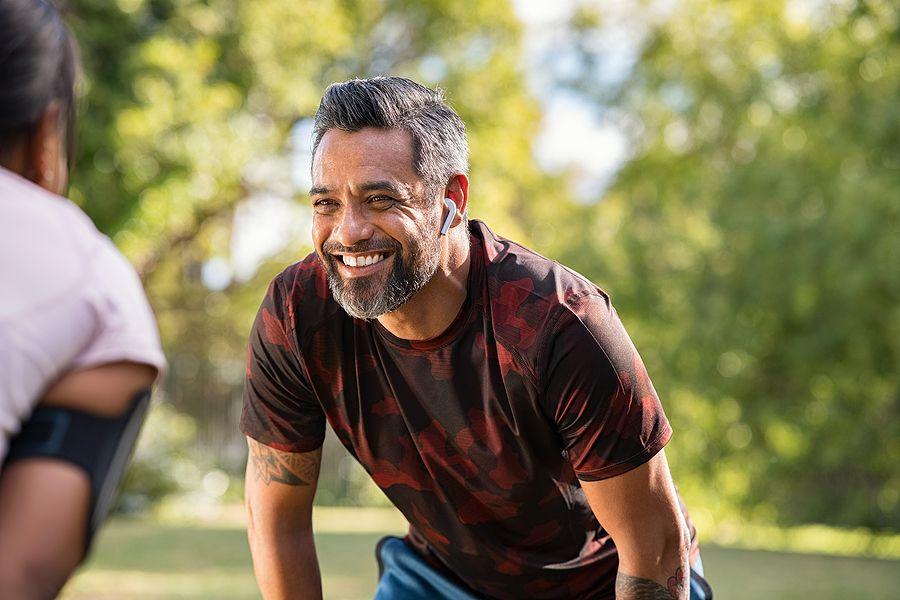 Happy mature fitness couple resting after a run in park. Smiling middle eastern man taking a break w