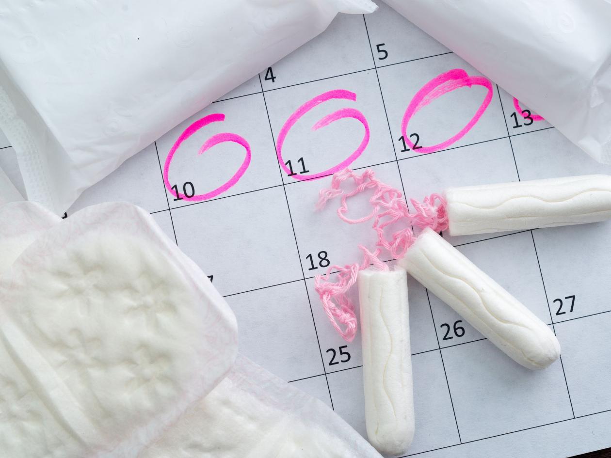 White calendar with pink circles around menstruation date period and clean tampons lying on top