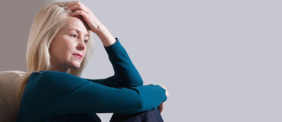 Woman Suffering From Stress Or A Headache Grimacing In Pain. Sad Depressed Woman At Home Sitting On